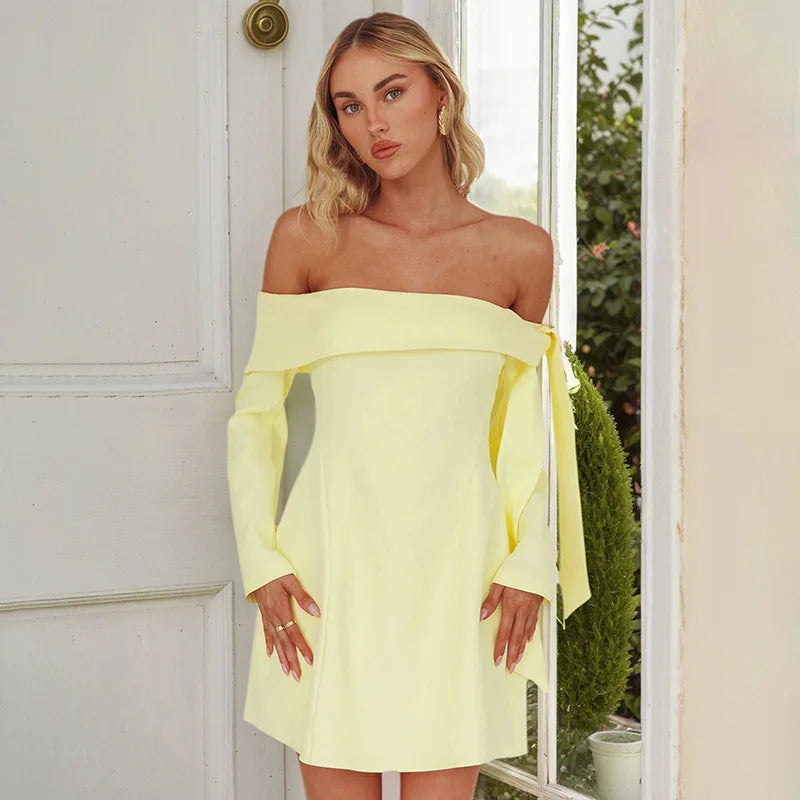 Woman wearing a light yellow off-shoulder dress standing in front of a white door.