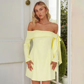 Woman wearing a light yellow off-shoulder dress standing in front of a white door.