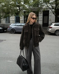 Woman in a brown jacket and gray pants standing on a street.