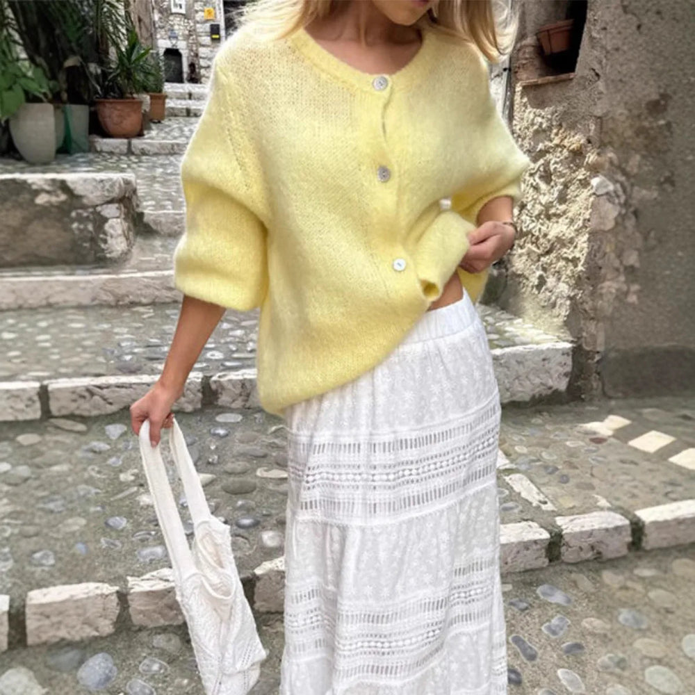 Person wearing a yellow cardigan and white lace skirt standing on stone steps.
