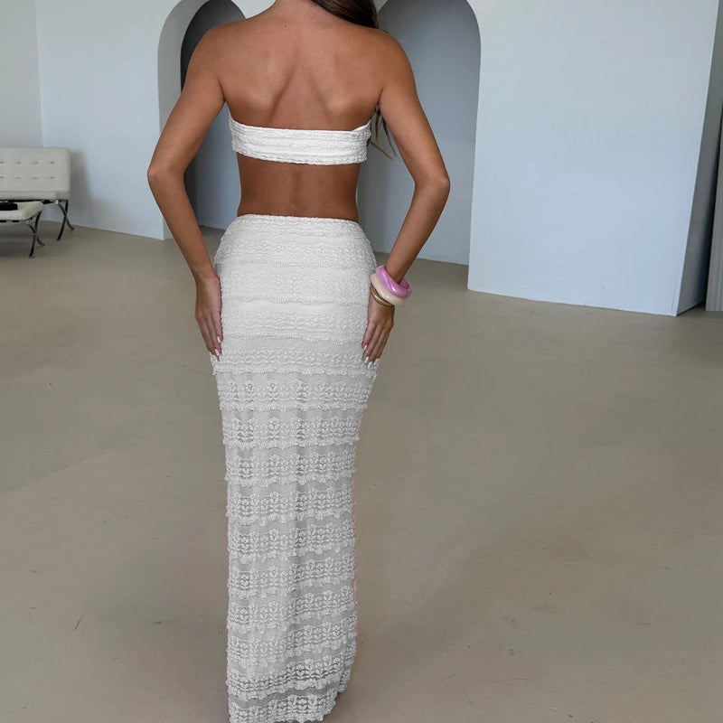 Woman wearing a white strapless top and long white skirt in an indoor setting.