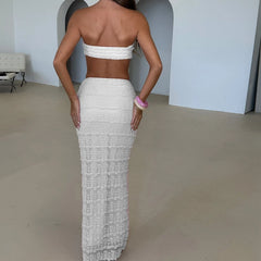Woman wearing a white strapless top and long white skirt in an indoor setting.