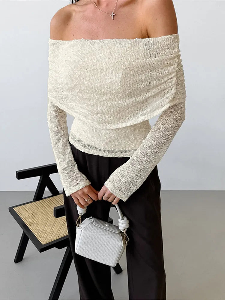 Person wearing a white off-shoulder top and holding a white handbag against a plain background