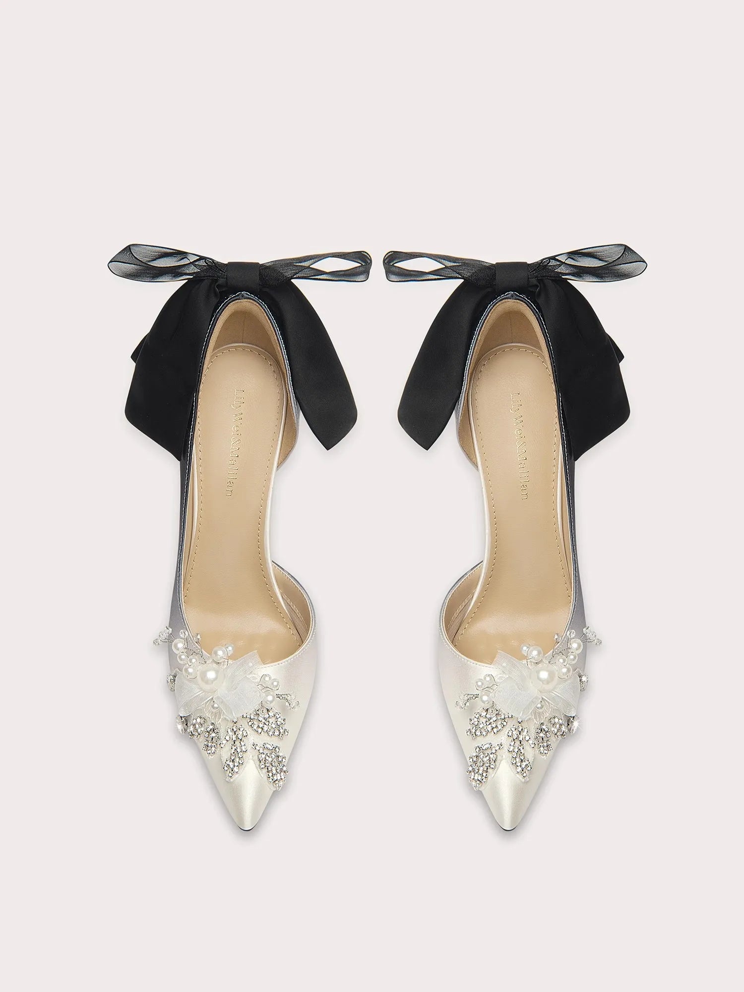 Pair of high-heeled shoes with black bows and pearl embellishments on a light gray background