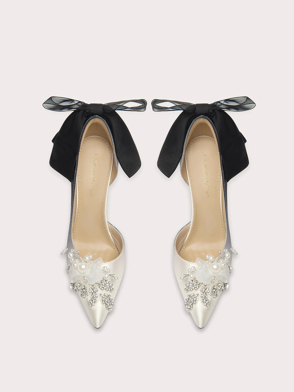 Pair of high-heeled shoes with black bows and pearl embellishments on a light gray background