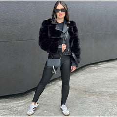 Woman wearing a black fur coat, black leggings, and white sneakers against a gray wall.