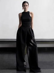 Person wearing a black sleeveless top and wide-leg pants against a plain background