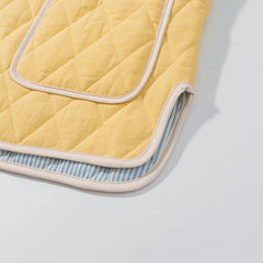 Yellow quilted baby blanket with blue and white striped lining on a light gray background