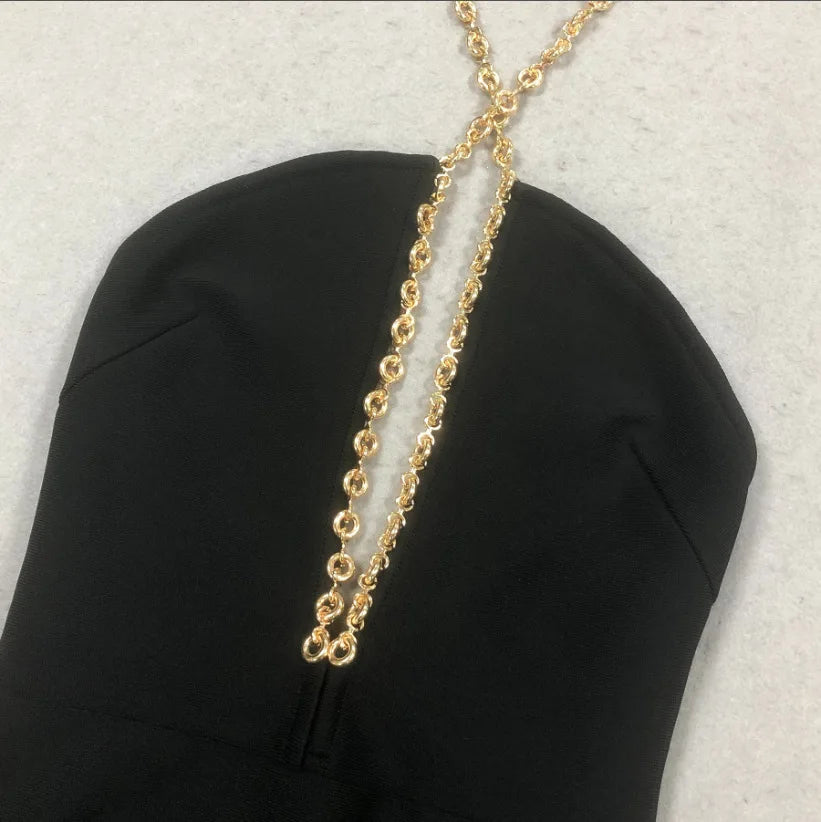 Gold chain necklace draped over a black garment on a light gray background