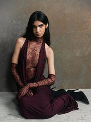 Woman wearing a burgundy dress with lace detailing and black gloves against a gray background