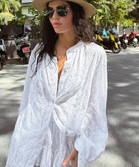Woman in a white outfit and hat standing on a street with parked motorcycles in the background