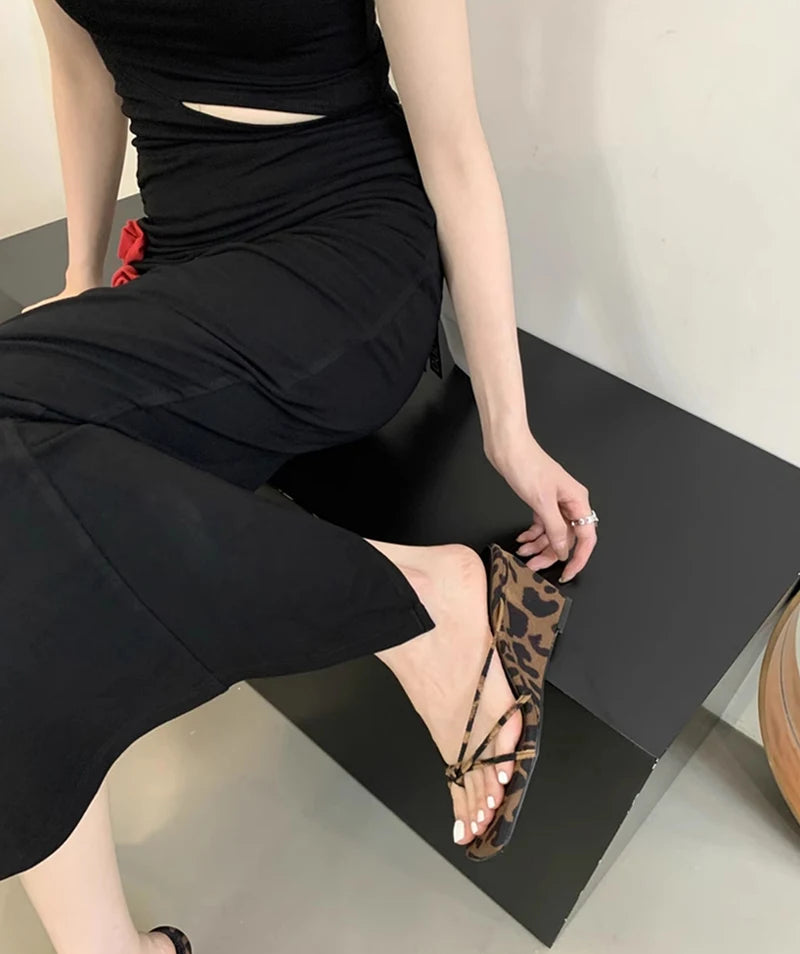 Person wearing a black outfit with a leopard print sandal on a black surface.