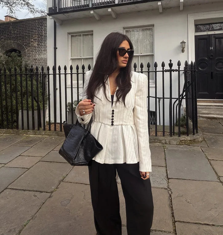 Woman in a white peplum jacket and black pants standing on a sidewalk.