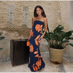 Woman in a blue strapless dress with orange floral patterns standing in front of a textured wall.