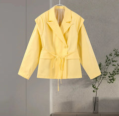 Yellow jacket hanging on a gray wall with a plant in the corner