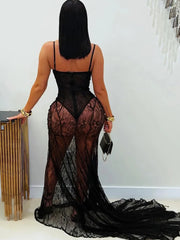 Woman wearing a black lace dress with sheer panels against a white wall.