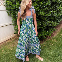 Woman wearing a green and blue patterned dress standing outdoors next to a hedge.