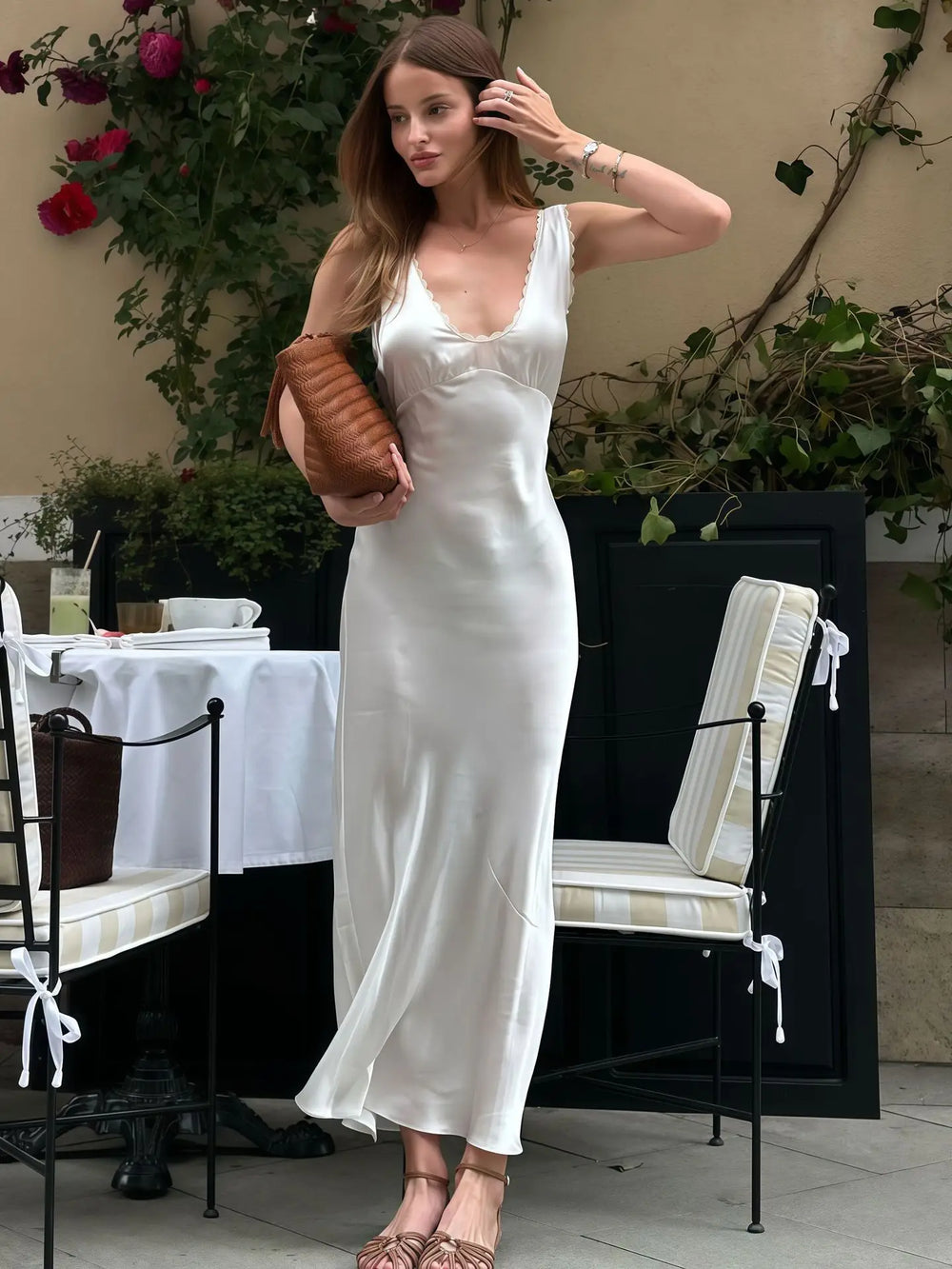 Woman in a white dress standing in an outdoor setting with tables and chairs.