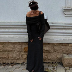 Woman in a black off-shoulder dress standing against a light-colored wall.