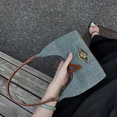 Hand holding a denim handbag with brown strap on a bench