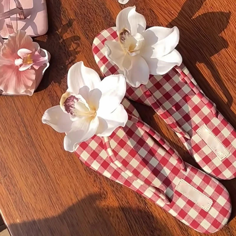Red and white checkered flip-flops with white flowers on a wooden surface