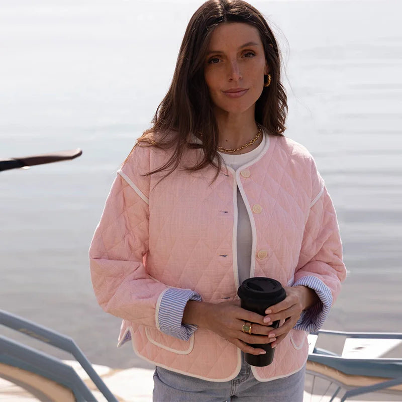 Woman wearing a pink quilted jacket holding a coffee cup outdoors.