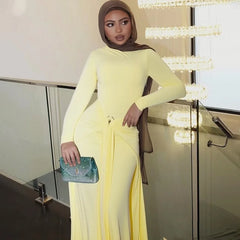 Woman in a yellow outfit holding a green clutch in an indoor setting.
