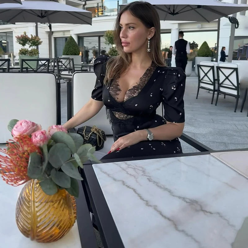 Woman in a black dress with lace details sitting at an outdoor cafe table with flowers.