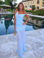 Woman in a light blue one-shoulder dress standing by a poolside.
