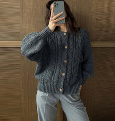 Person wearing a dark gray knitted cardigan with wooden buttons against a wooden wall.