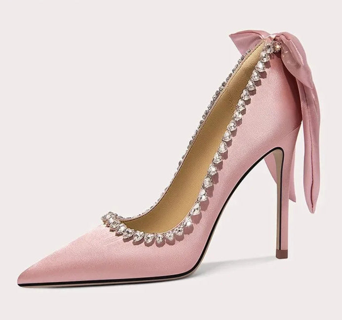 Pink high-heeled shoe with decorative bow and crystals on a white background