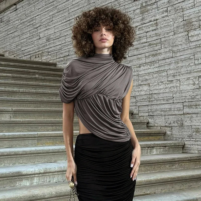 Woman wearing a brown draped top and black skirt standing on stone steps with a stone wall background