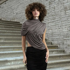 Woman wearing a brown draped top and black skirt standing on stone steps with a stone wall background