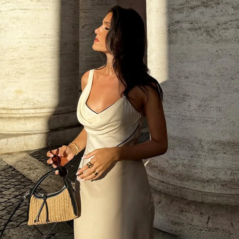 Woman in a white dress standing against a stone wall with a woven bag.