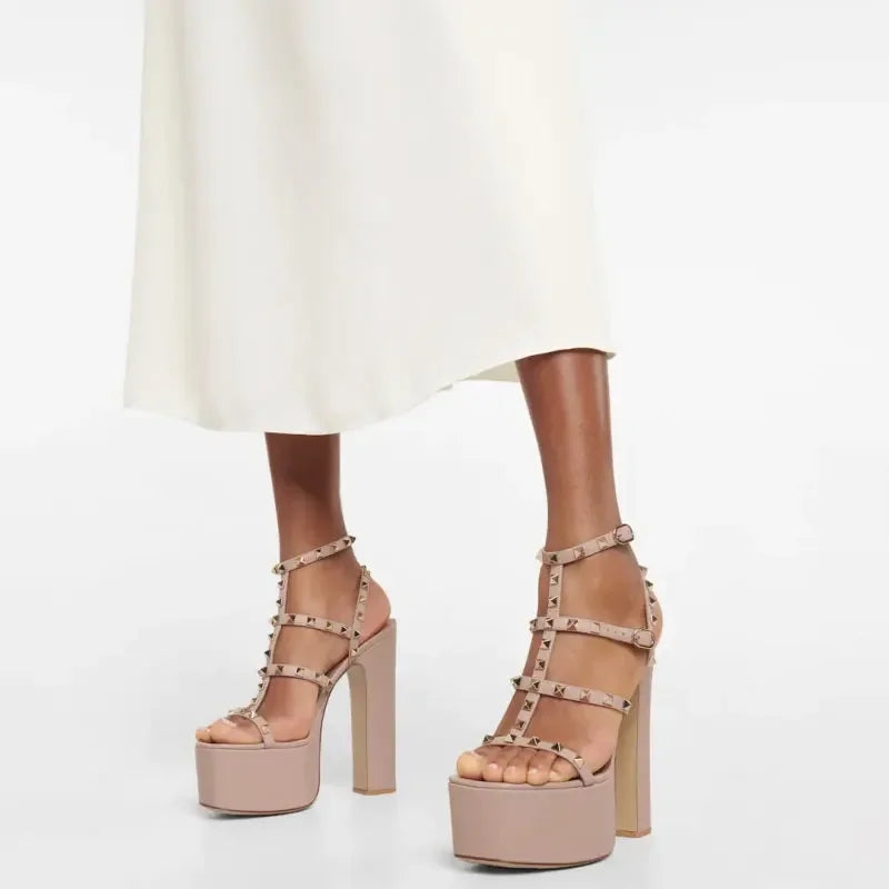 Beige platform sandals with studded details worn with a white skirt on a light gray background