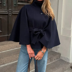 Person wearing a navy blue cape with a bow detail, standing on steps.