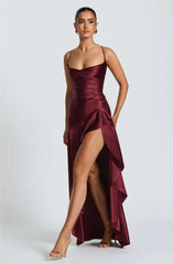 Woman wearing a burgundy evening gown with a high slit on a white background