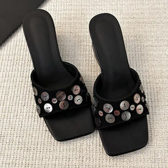 Top-down view of black square toe wedge heel slide sandals with decorative shell buttons.