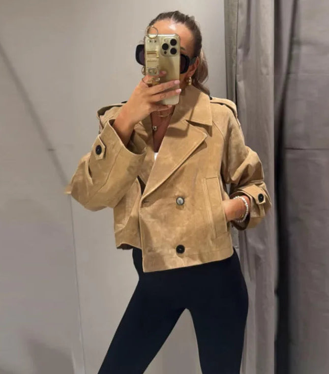 Person wearing a beige jacket taking a mirror selfie.