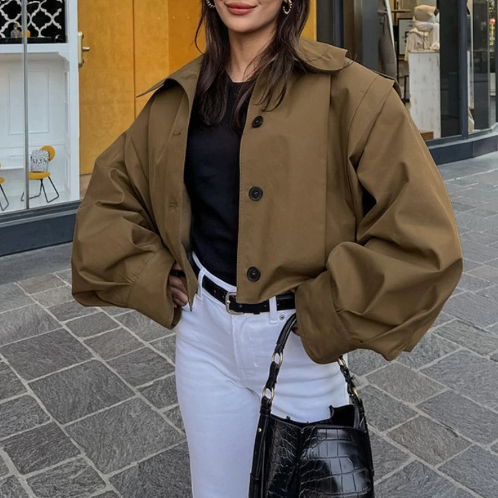 Woman wearing a brown jacket, black top, and white pants on a city street.