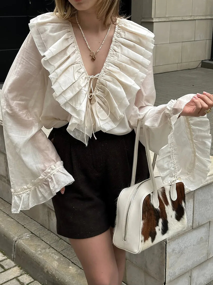 Person wearing a white ruffled blouse and black shorts, holding a cowhide-patterned handbag.