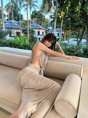 Woman in a beige dress sitting on a couch with palm trees and buildings in the background