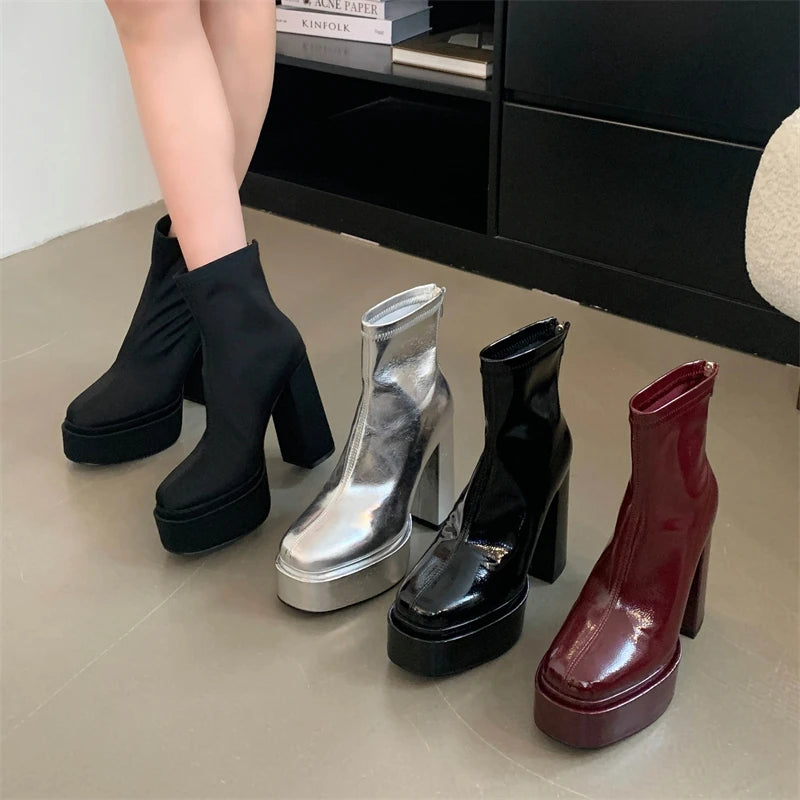 Four pairs of high-heeled boots in black, silver, and red on a light gray floor.