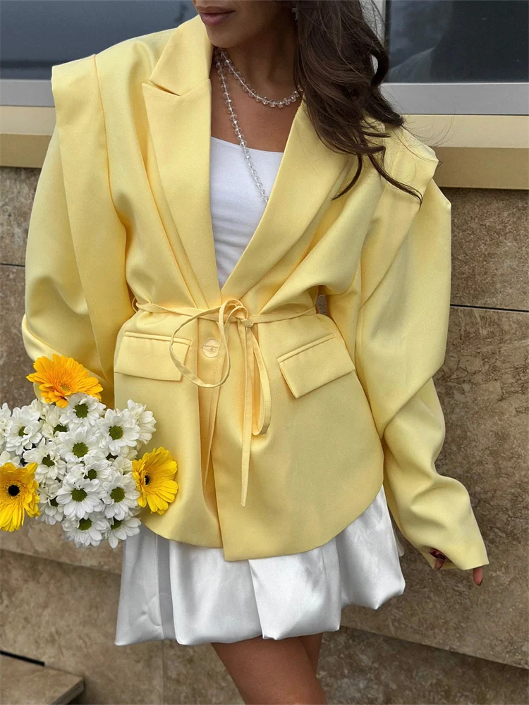 Person wearing a yellow blazer holding flowers against a neutral background