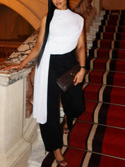 Model on stairs wearing asymmetric draped neck sleeveless white top