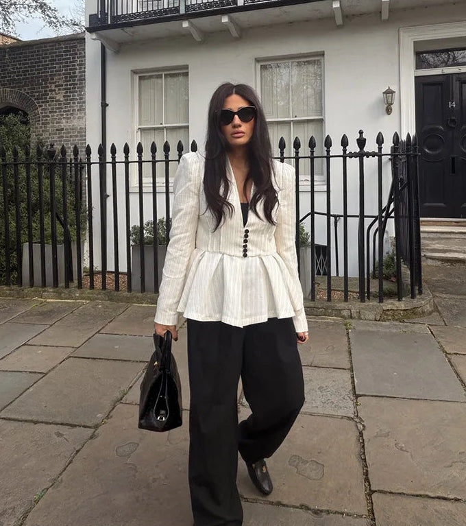 Woman in a white peplum top and black pants walking on a pavement.