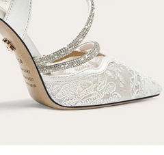 White high-heeled shoe with lace detailing and a decorative strap on a white background