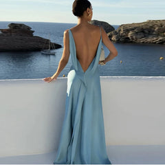 Woman in a light blue evening gown with an open back, standing by a scenic waterfront.