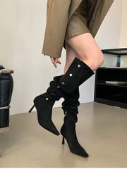 Person wearing black knee-high boots with high heels in a minimal indoor setting.