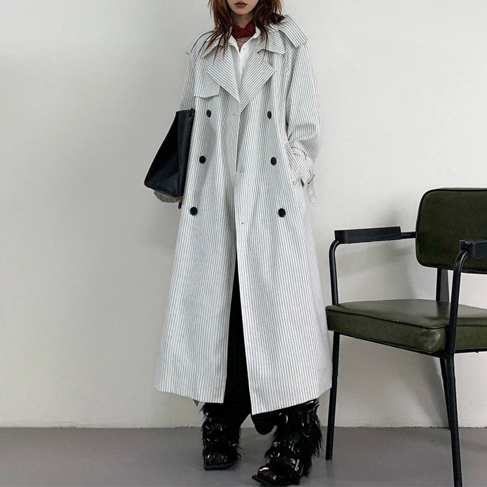 Person wearing a long black and white striped coat in a minimalistic setting with a chair.